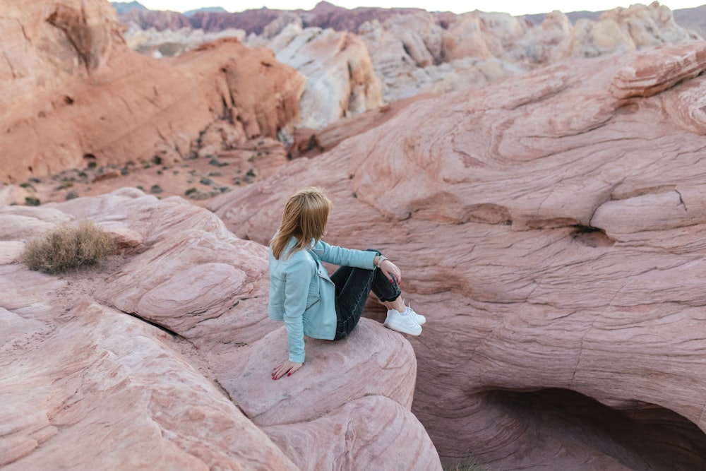 woman in blue jacket sitting on brown rock formation during daytime
