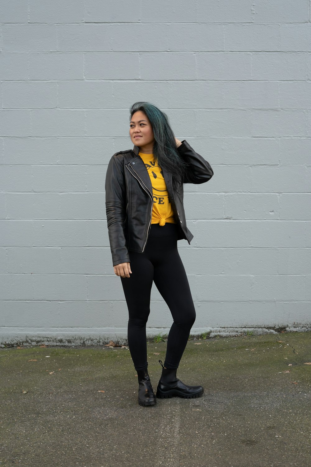 woman in black jacket and black pants standing beside white wall