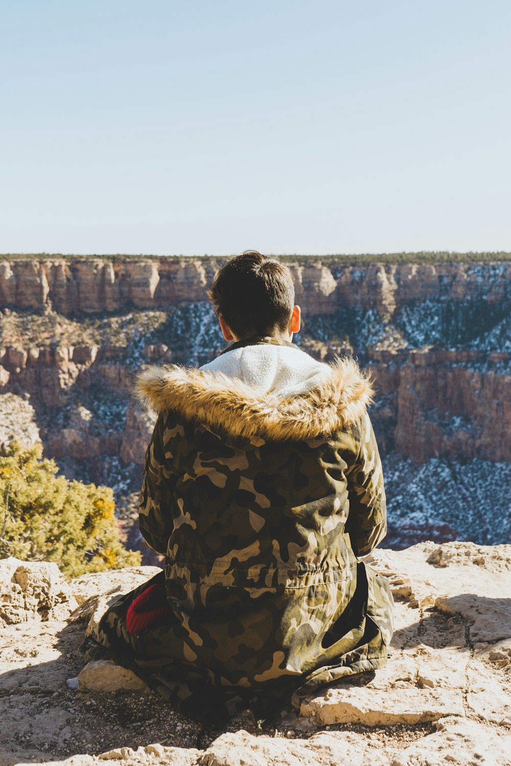 man in brown and black jacket sitting on rock looking at the city during daytime