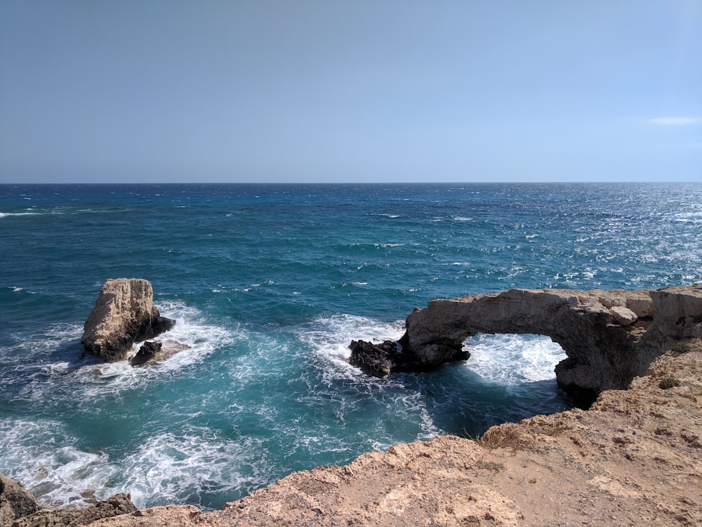 brown rock formation on sea under blue sky during daytime