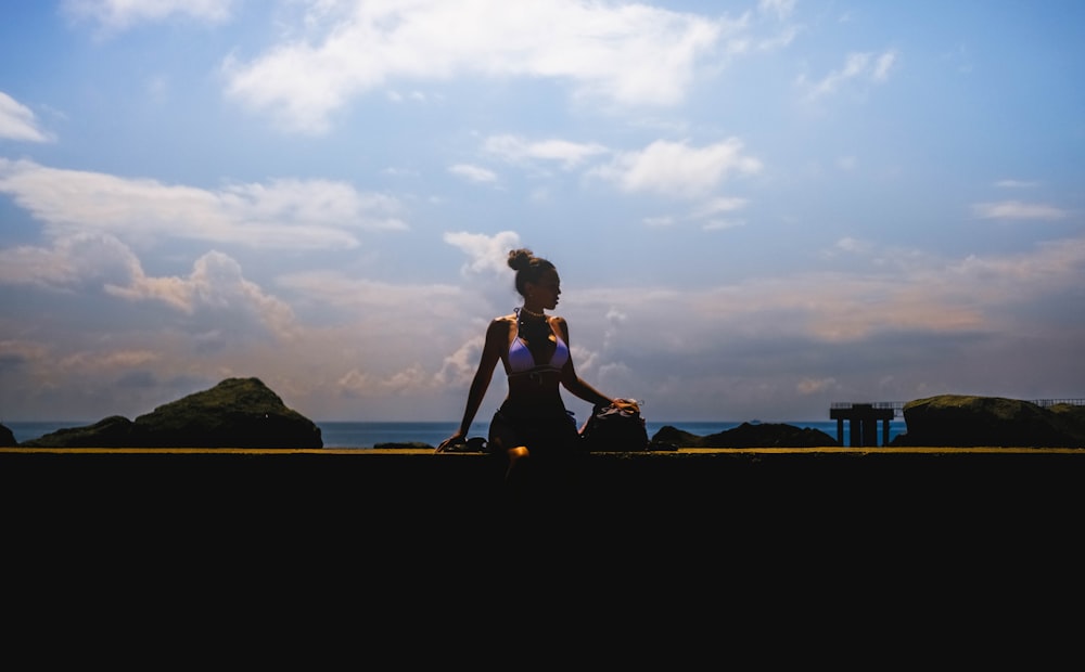 woman in black tank top and black pants sitting on brown wooden fence during sunset