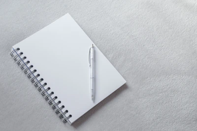 Close-up of a minimalist guided journal open on a white desk with a soft pastel pen beside it.