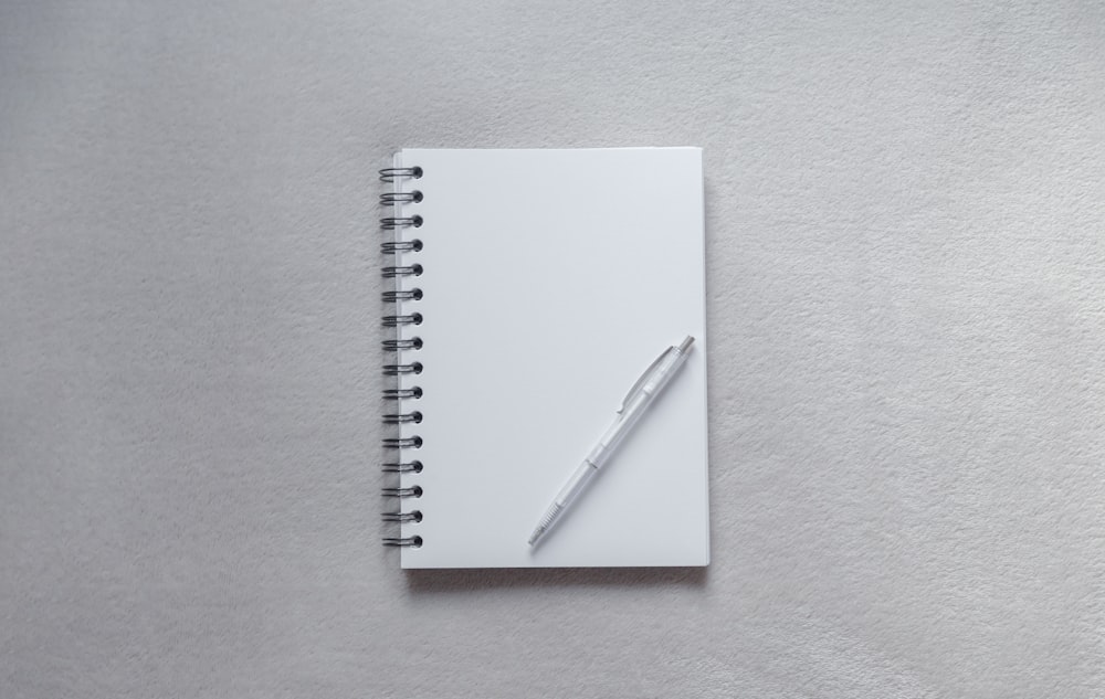 Weißes Notizbuch mit Stift auf hellem Untergrund