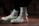 A pair of off-white high-top sneakers with a distinctive red and black design on the side, worn with white socks featuring a black logo. The shoes are on a brown surface, and the lighting creates a moody and stylish atmosphere.
