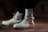 A pair of off-white high-top sneakers with a distinctive red and black design on the side, worn with white socks featuring a black logo. The shoes are on a brown surface, and the lighting creates a moody and stylish atmosphere.