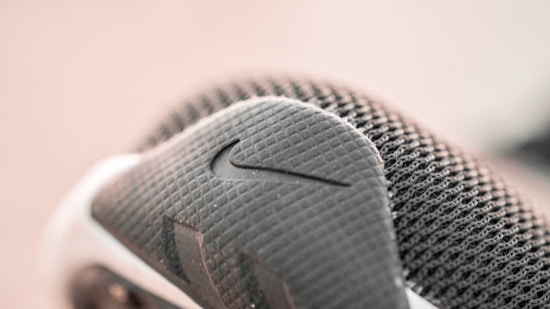 Close-up view of a textured sneaker, featuring a mesh fabric and a prominent swoosh logo. The shoe displays intricate detailing in shades of gray and white.