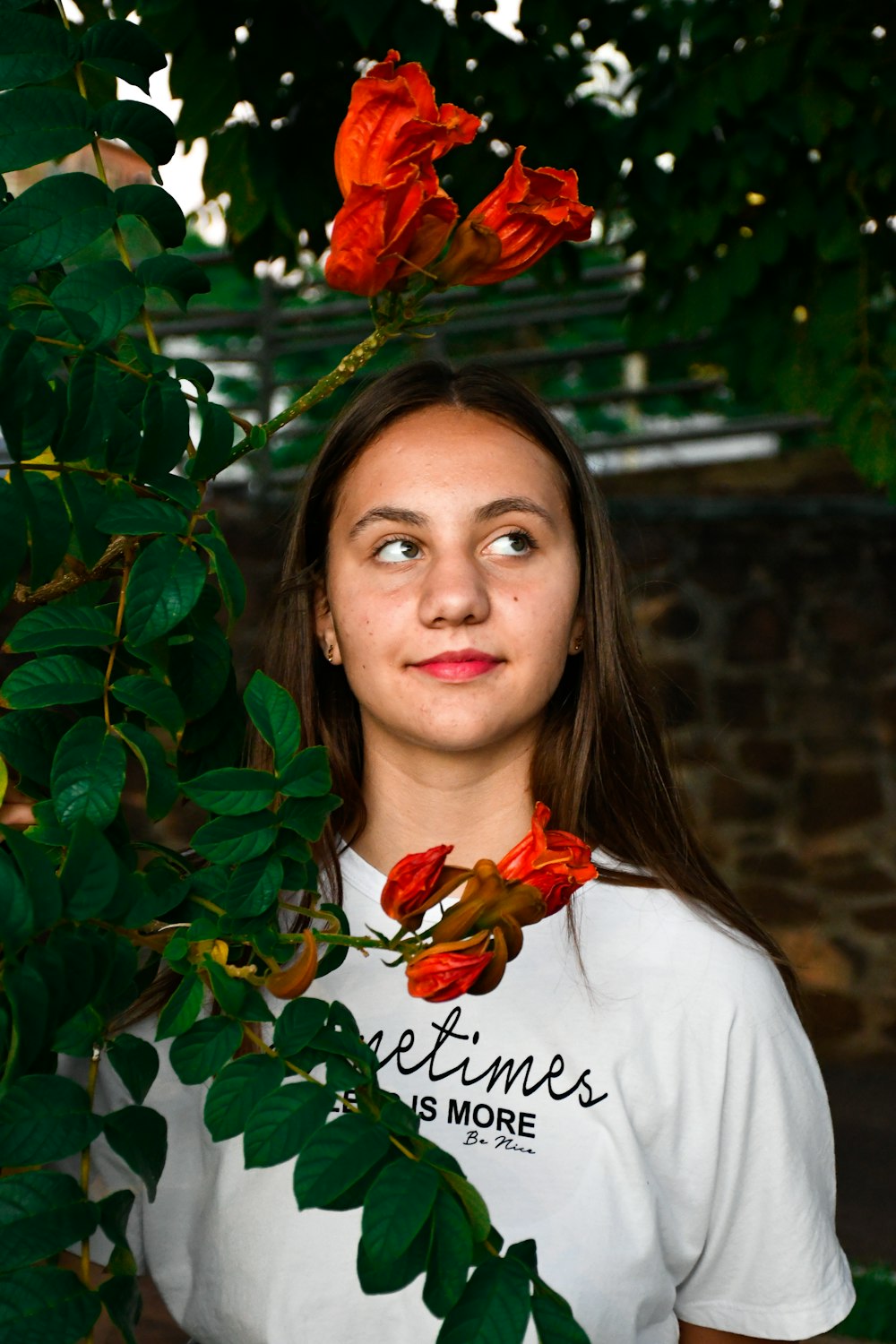 woman in white shirt standing beside red flowers