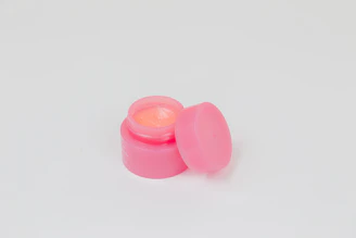 Pink lip balm jar lid on a white surface