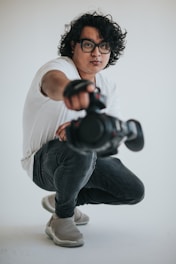 man in white crew neck t-shirt and blue denim jeans holding black dslr camera