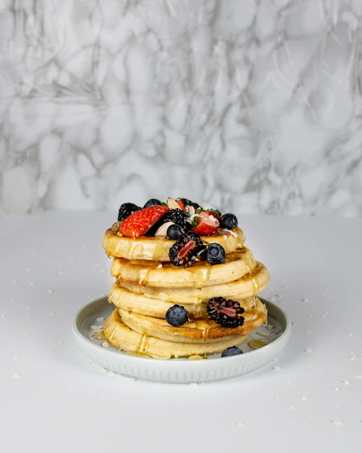 A stack of fluffy, golden protein pancakes drizzled with natural honey and fresh strawberries on a rustic wooden table.