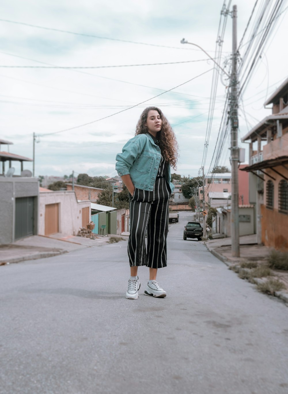 woman in teal long sleeve shirt and black skirt standing on gray concrete road during daytime