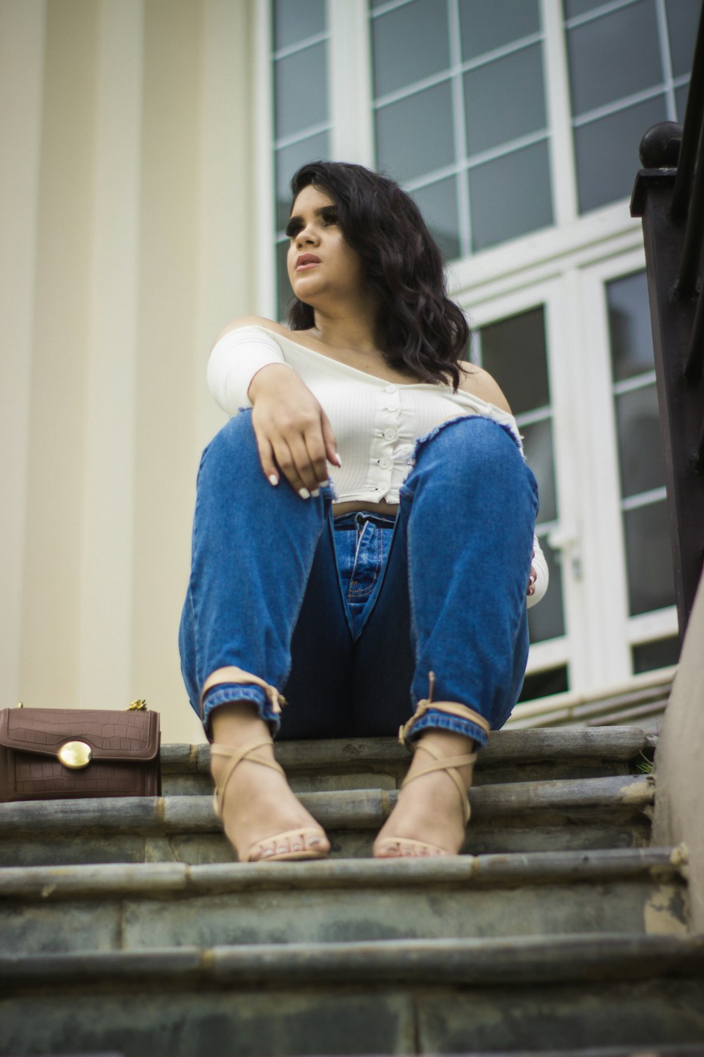 woman in white long sleeve shirt and blue denim jeans sitting on brown wooden bench