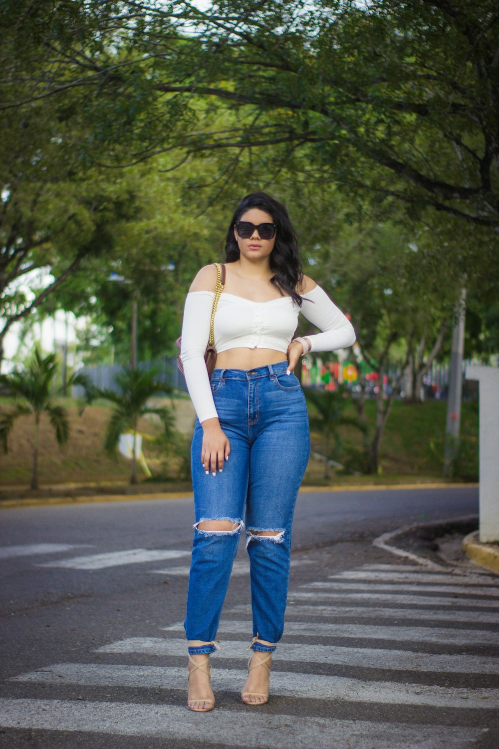 woman in white spaghetti strap top and blue denim jeans standing on road during daytime