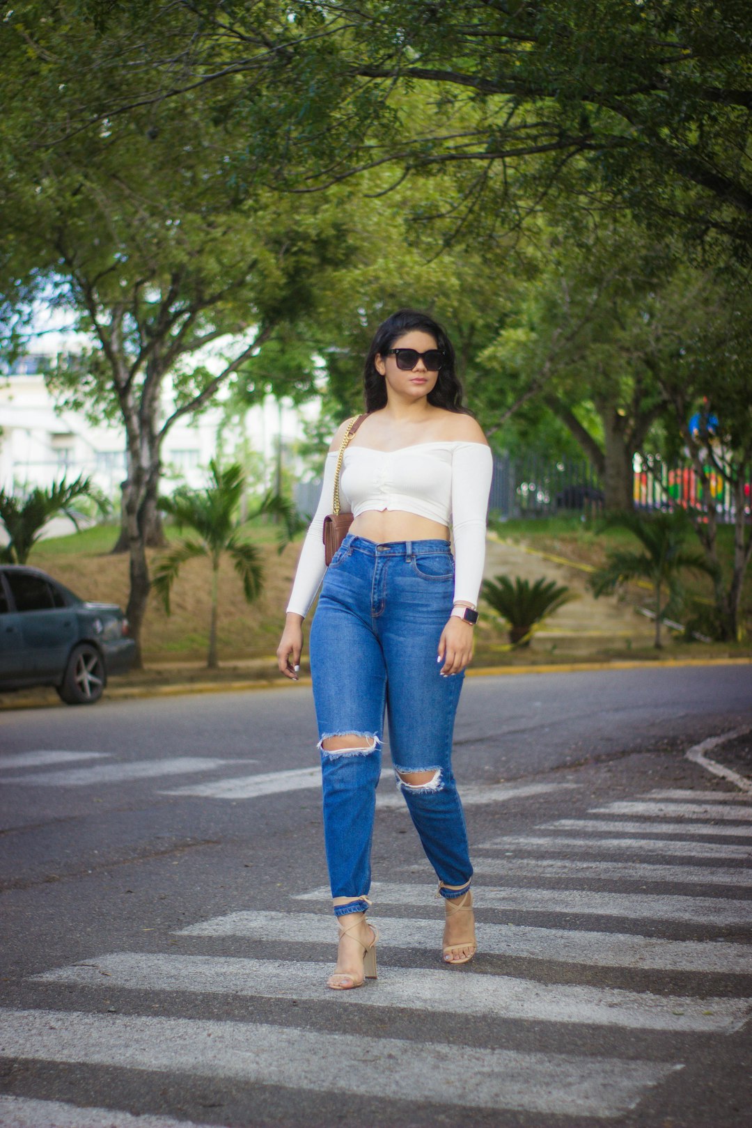 woman in white tank top and blue denim jeans standing on road during daytime