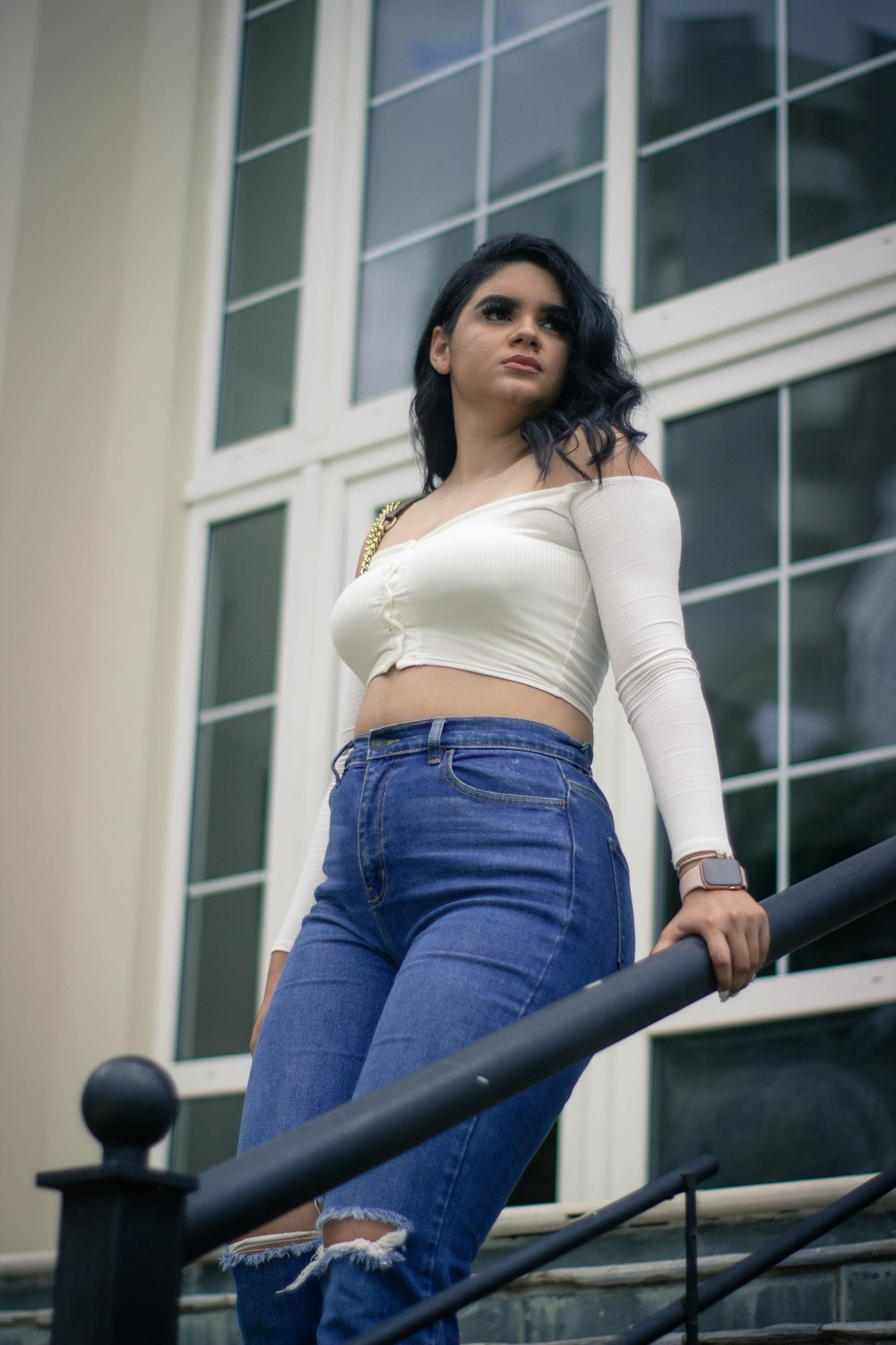 Femme en chemise blanche à manches longues et jean en denim bleu appuyée sur des balustrades en métal noir