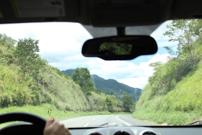 A winding road through lush green hills captured from the car window.