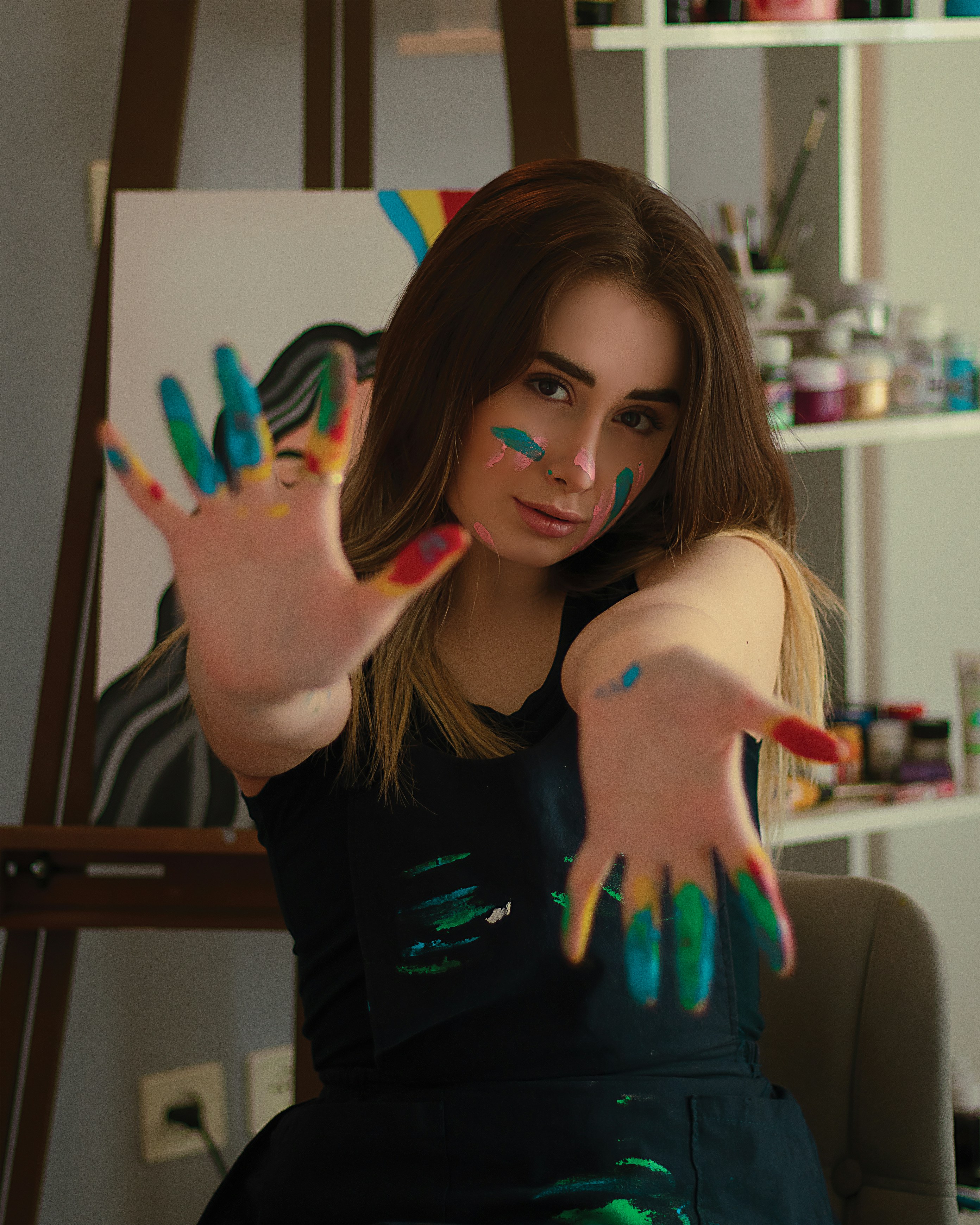 Artist in studio, dim warm lighting, paint on hands, dark atmospheric environment, deep shadows