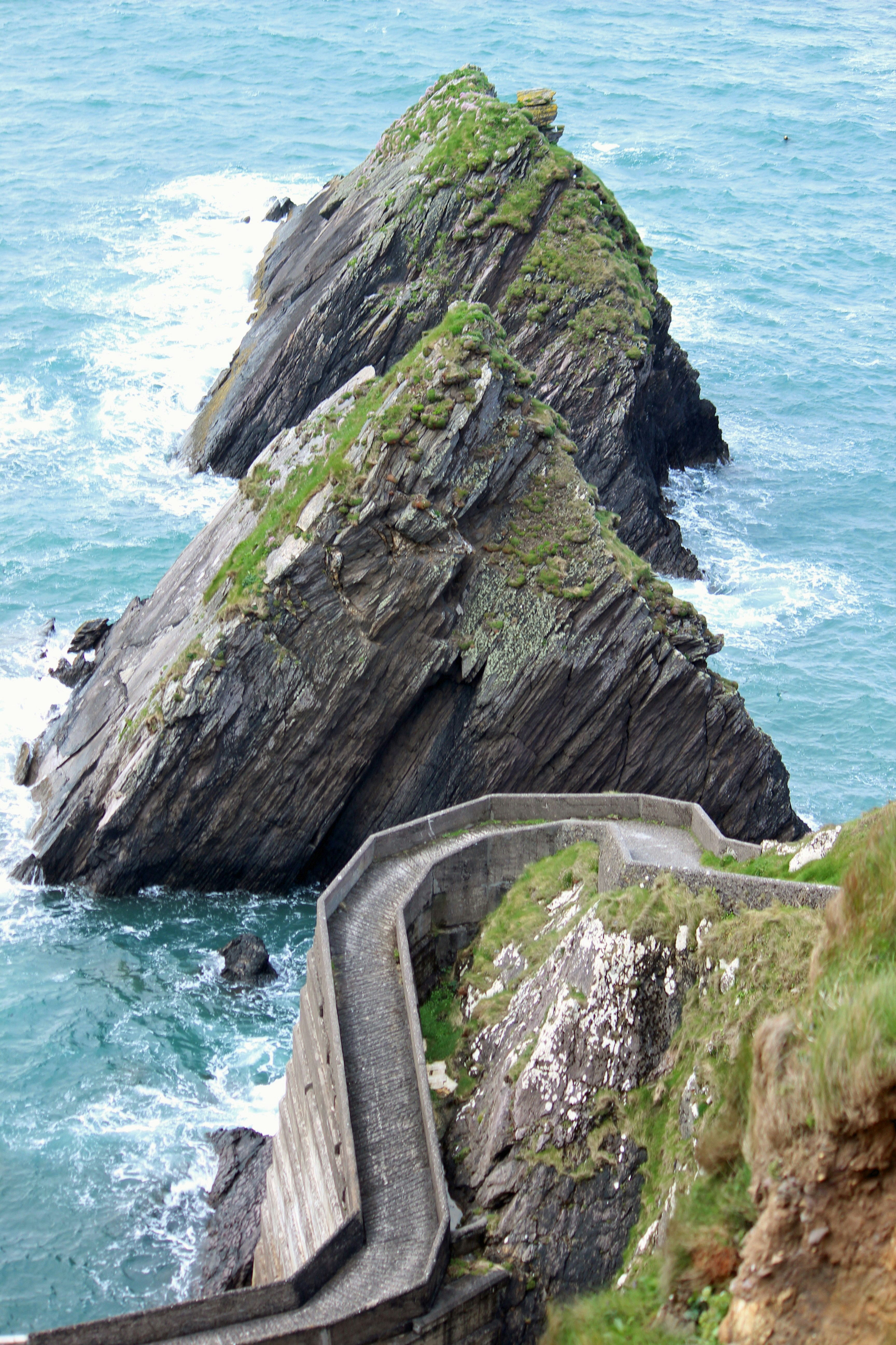 gray concrete road on green mountain beside body of water during daytime