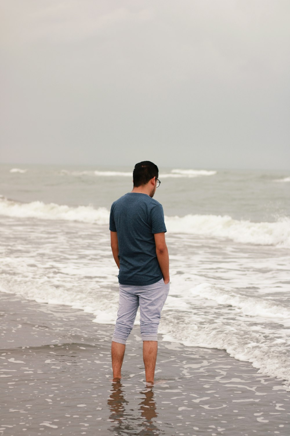青いTシャツと白い短パンを着た男が昼間、ビーチに立っている
