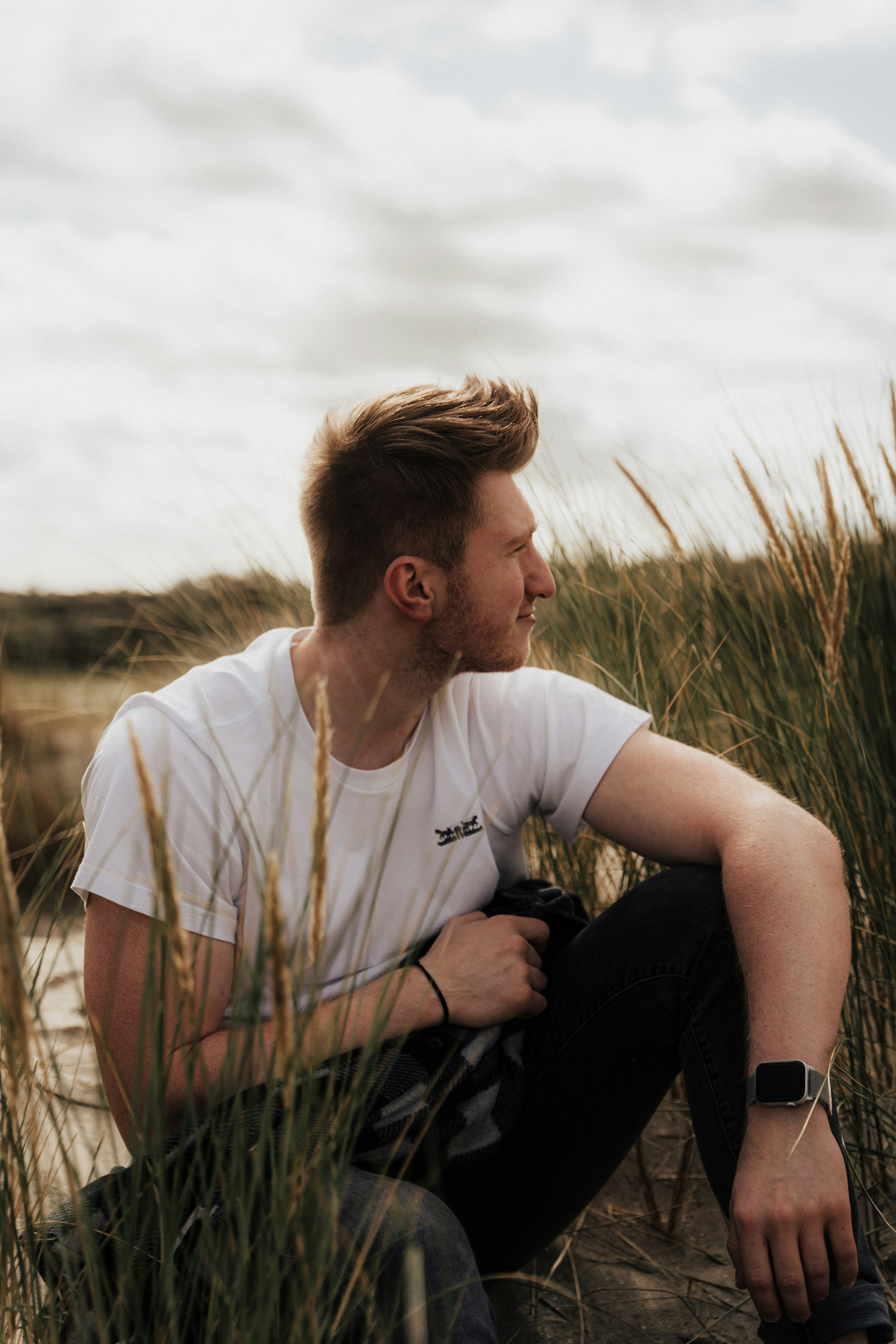 man in white crew neck t-shirt sitting on grass field during daytime