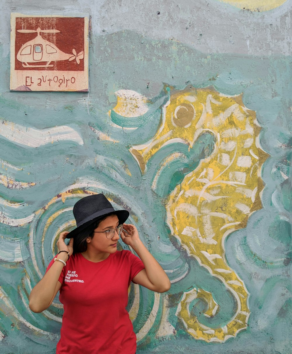 빨간 티셔츠와 검은 모자를 쓴 여자가 낙서로 벽에 기대어 있다