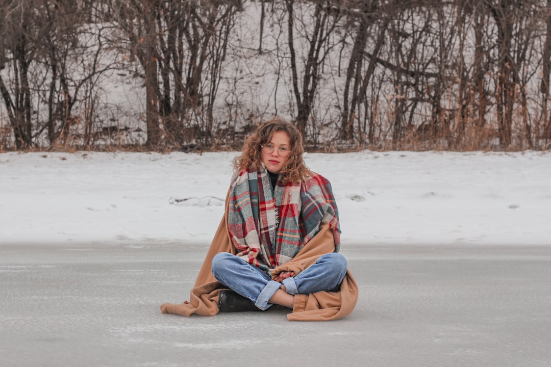 woman in red and black plaid scarf sitting on snow covered ground during daytime
