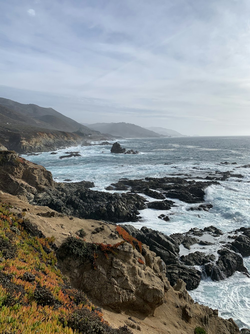 brown rocky mountain beside sea under white clouds during daytime