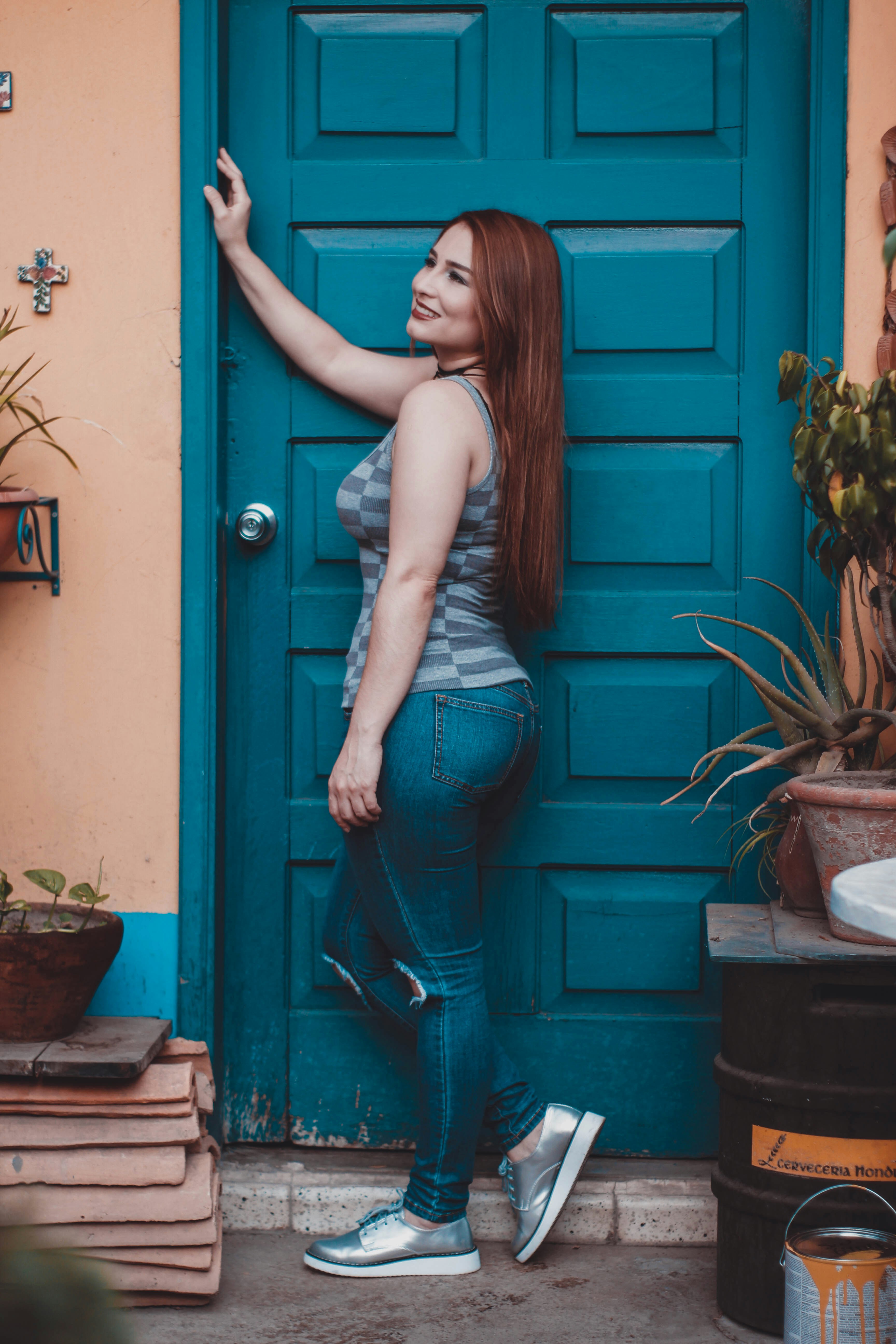 woman in gray tank top and green pants standing beside blue wooden door