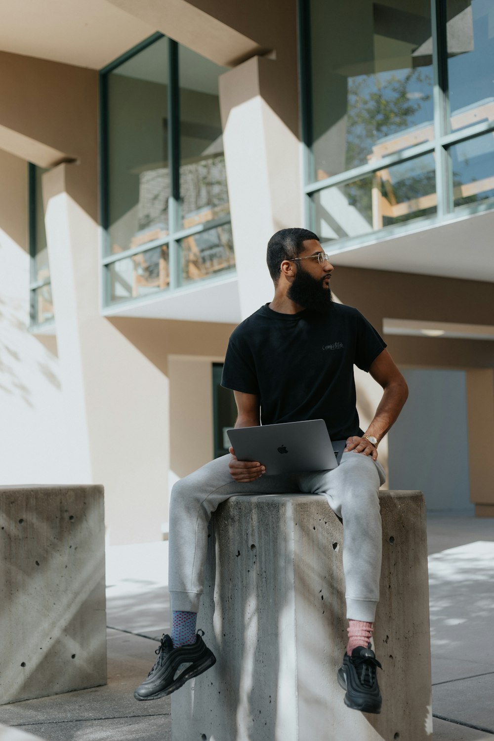 man in black crew neck t-shirt sitting on white concrete bench using macbook