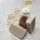 A clear plastic bottle filled with amber-colored liquid is positioned next to two bars of textured beige soap. Oats are scattered across the light stone surface, providing a rustic and natural setting.