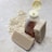 A clear plastic bottle filled with amber-colored liquid is positioned next to two bars of textured beige soap. Oats are scattered across the light stone surface, providing a rustic and natural setting.