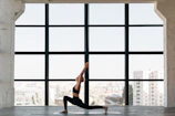 A serene morning class practicing slow Hatha yoga stretches by large windows.