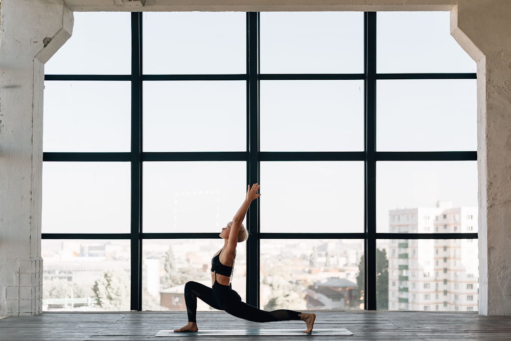 Frau in schwarzem Tanktop und schwarzen Leggings beim Yoga