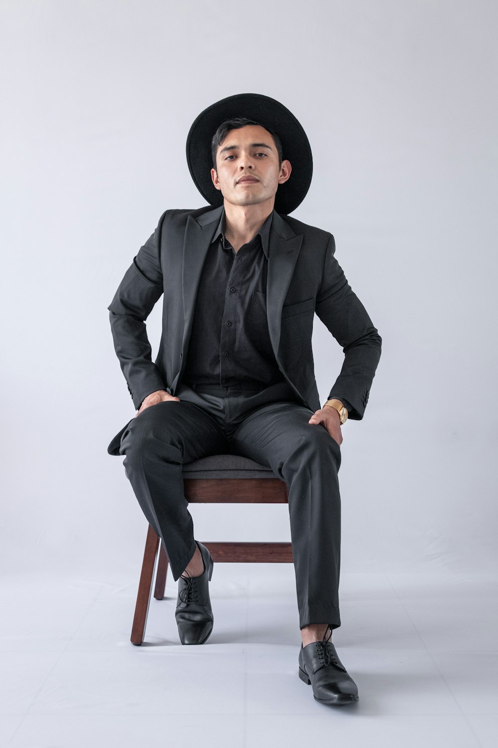 man in black suit jacket and black pants sitting on brown wooden chair