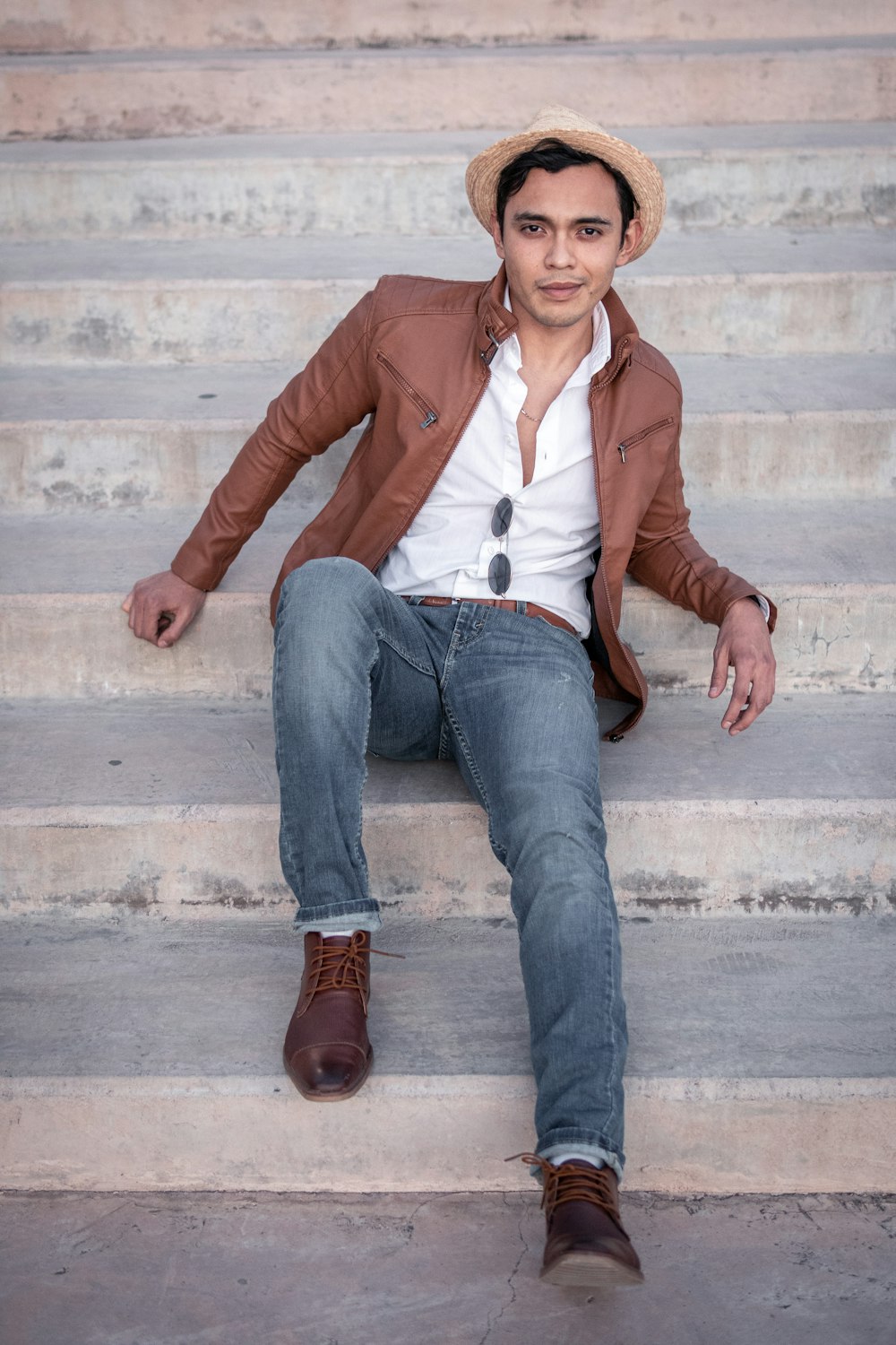 woman in brown leather jacket and blue denim jeans sitting on concrete stairs