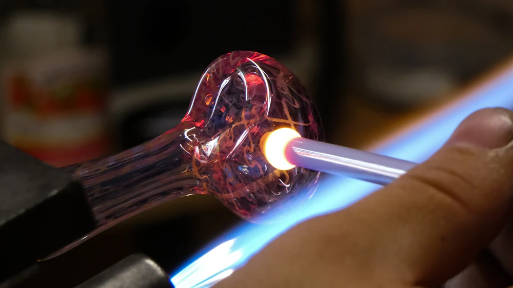 An artist working glass on a bench torch, wide studio shot