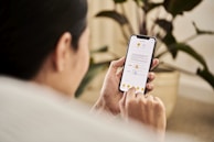 A person holding a smartphone and interacting with a mobile app that displays a document. The individual is sitting indoors, likely in a relaxed setting with a houseplant visible in the background.