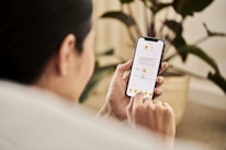 A person holding a smartphone and interacting with a mobile app that displays a document. The individual is sitting indoors, likely in a relaxed setting with a houseplant visible in the background.