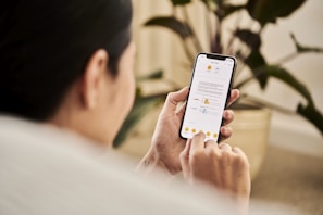 A person holding a smartphone and interacting with a mobile app that displays a document. The individual is sitting indoors, likely in a relaxed setting with a houseplant visible in the background.