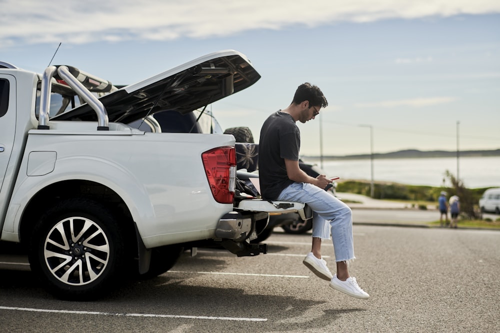 man sitting on car looking at phone