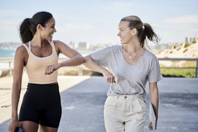 woman in gray shirt elbow bumping with woman in sports outfit