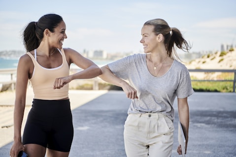 woman in gray shirt elbow bumping with woman in sports outfit