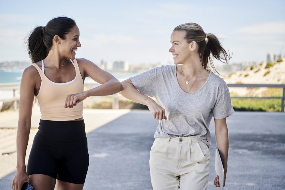 woman in gray shirt elbow bumping with woman in sports outfit