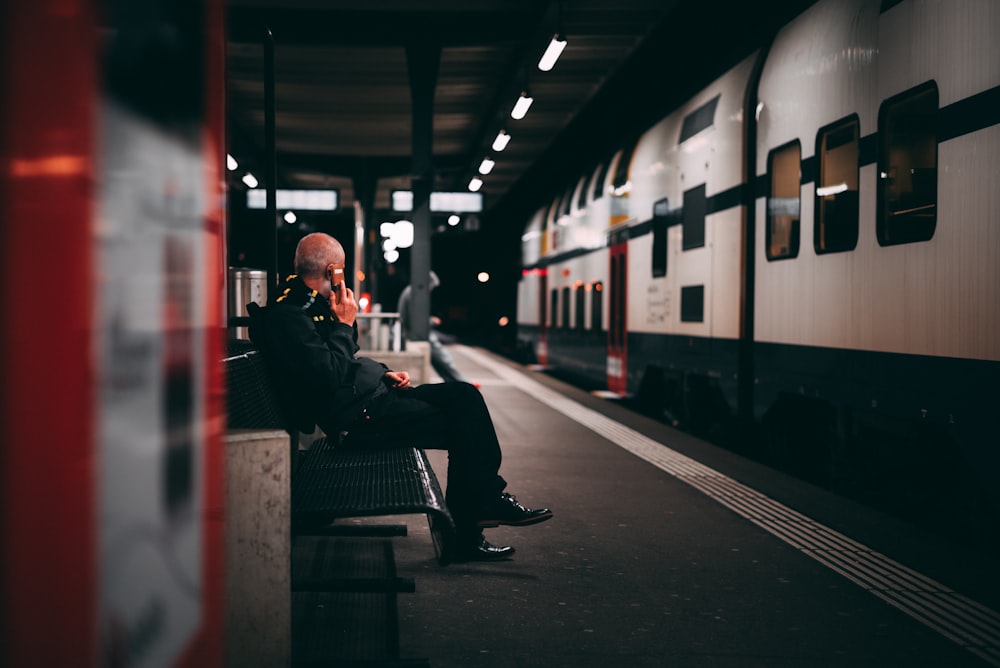 man in black jacket sitting on bench in train station