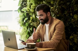 man in brown jacket sitting at a table looking at laptop