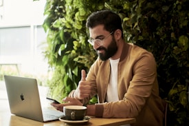 man in brown jacket sitting at a table looking at laptop