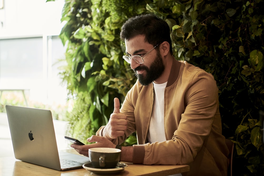 man in brown jacket sitting at a table looking at laptop