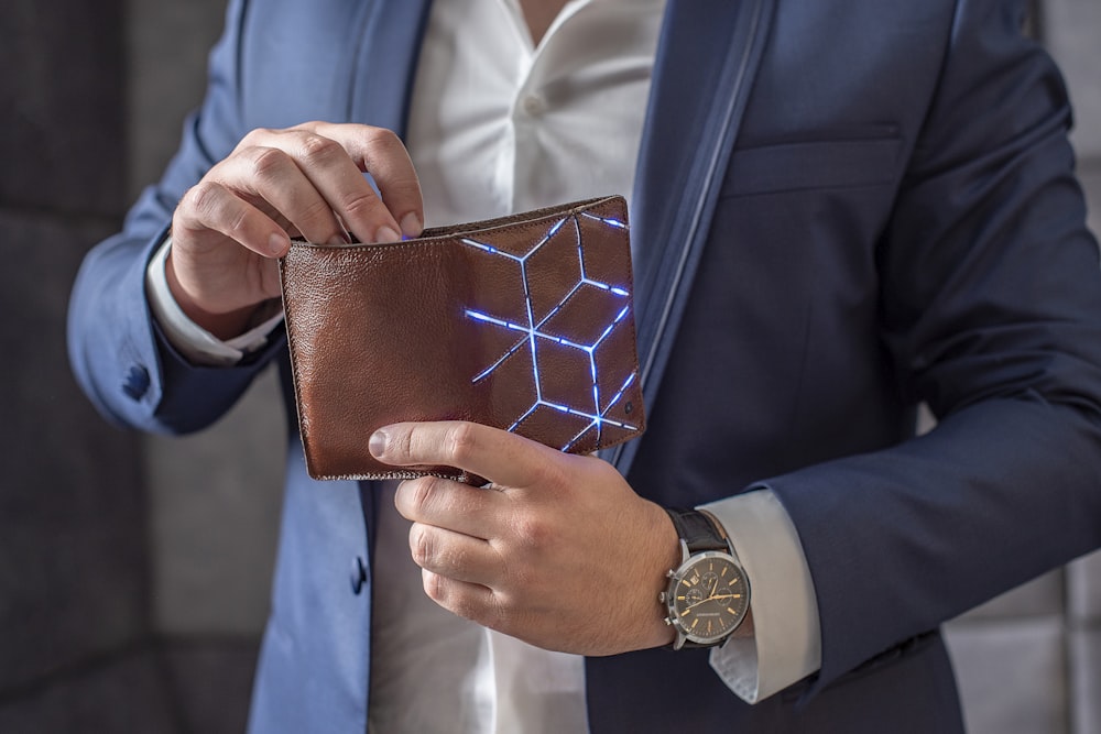 man in blue suit jacket holding brown leather wallet