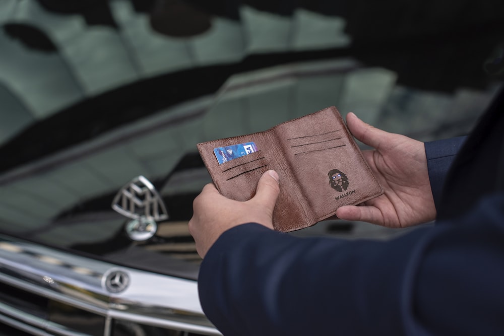 person holding brown leather bifold wallet