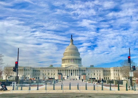 people walking on street near white concrete building under blue and white cloudy sky during daytime